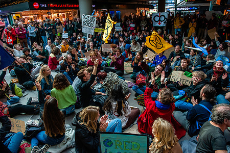 Climate activists are seen sitting on the ground of the main hall of the airport during the demonstration. Hundreds of climate activists gathered outside of Schiphol to demand a climate plan for the airport. The activists marched through the main hall inside the airport, and walked to the construction site where a new terminal of Schiphol is to be built. After that, they went back and ocuppied the main hall for a few hours, while other activists outside blocked several private jets, because according to Greenpeace, flights with those planes are the most polluting. The disrupted mass action was organized by Greenpeace Netherlands and Extinction Rebellion.