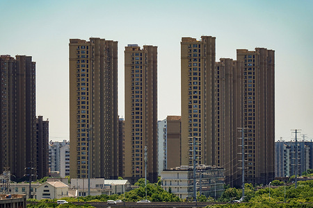 High rise residential towers in brown tones, with a mix of other buildings, utility poles, and a road with vehicles in the foreground.