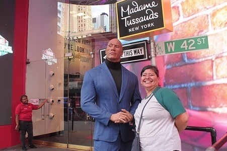 A person stands next to a model figurine of "The Rock" Dwayne Johnson in front of Madame Tussauds wax museum on 42nd Street in Manhattan.