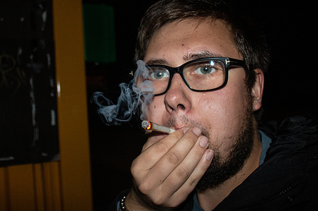 A man smokes a joint outdoors at night.
