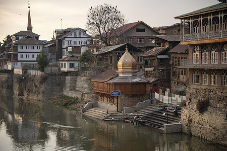 Cloth washers clean garments beside a temple in downtown Srinagar during sunset.