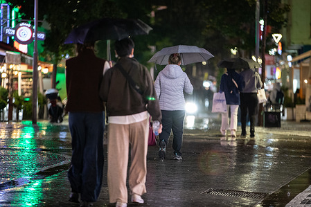 People walking on the street shelter underneath umbrellas during rainfall.