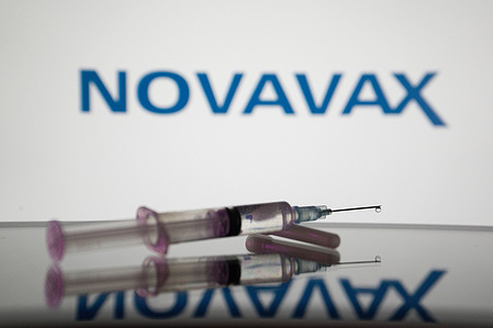 In this photo illustration, a medical syringe is displayed on a screen, and the logo of Novavax in the background.
