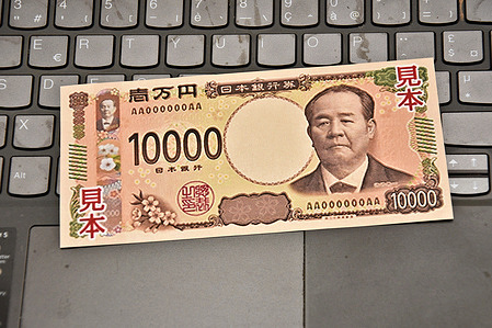 In this photo illustration, a sample of the new Japanese 10,000 yen banknote is placed on the keyboard of a laptop. Starting July 3, 2024, the Bank of Japan will release a new series of banknotes to financial institutions, which will then distribute them over their counters and through ATMs. Financial institutions will begin distribution after completing the necessary preparations. The new 1,000, 5,000, and 10,000 yen notes are designed to reduce the risk of counterfeiting, with enhanced security features introduced by the Ministry of Finance and the Bank of Japan.