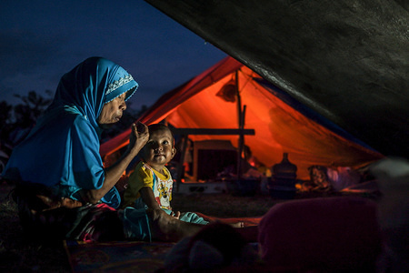 A grandmother is nursing her granddaughter in the Lere Refugee settlement.
A deadly earthquake measuring 7.7 magnitude and the tsunami wave caused by it has destroyed the city of Palu and much of the area in Central Sulawesi. According to the officials, death toll from devastating quake and tsunami rises to 1,347, around 800 people in hospitals are seriously injured and some 62,000 people have been displaced in 24 camps around the region.