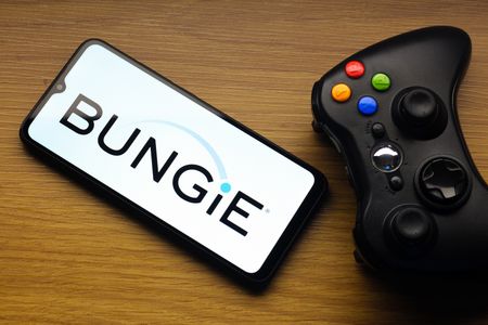 In this photo illustration, the Bungie logo is seen displayed on a smartphone screen next to an Xbox video game controller.