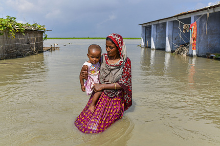 A woman carries her child through a flooded street in Bogura.
One third of Bangladesh is under water after heavy rains hit the nation. At least 1.5 million people have been affected, with homes and roads in villages flooded. Flood Forecasting and Warning Centre (FFWC) officials have reported, the flood situation in 15 northern and central districts has been due to the rise in water levels of the main rivers, including the Brahmaputra, Jamuna, Padma, Teesta and Dharla.