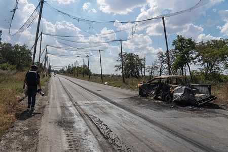 A journalist walks past the wreckage of a vehicle on a main road covered with anti-drone netting. The city of Druzhkivka in Ukraine’s eastern Donetsk region is being battered by Russian strikes as the front line moves closer. Druzhkivka is one of four frontline cities that form part of what Ukraine calls its “fortress belt.”