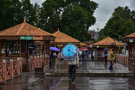 Commuters hold umbrellas as they walk along the wooden foot-bridge during rainfall. Jammu and Kashmir remained in the grip of a prolonged wet spell for the sixth consecutive day with heavy rainfall triggering cloudbursts, flash floods, rising river levels, rescue operations and widespread disruption across the valley. While the River Jhelum crossed the flood declaration mark, authorities activated flood response measures and urged the public not to panic.