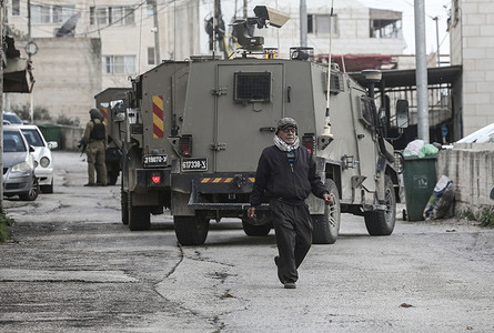 A Palestinian man walks past Israeli military vehicles during a military operation. Israeli forces surrounded a Palestinian home in West Bank city of Nablus during a military operation in the Halawa neighborhood of Nablus.