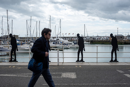 A member of the public walks by the silhouettes at the Ramgate Harbour. Standing with Giants silhouettes installed at Ramsgate Harbour, UK to honour town’s wartime role. The temporary installation of 338 life size soldiers, one to represent every 1000 rescued from the beaches in Dunkirk, France in Operation Dynamo in 1940.