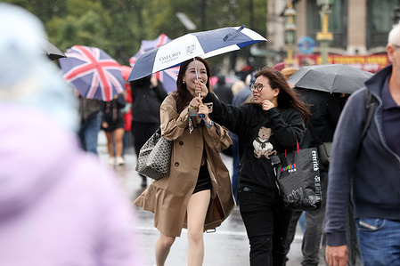 Women on Westminster Bridge in London under an umbrella during a rainy day.