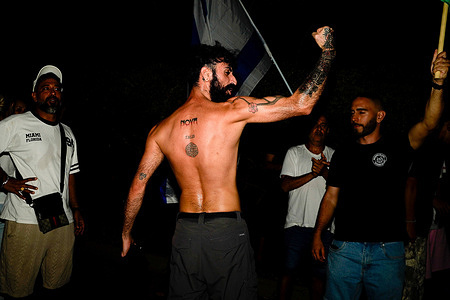A protester who survived the Nova music festival seen showing his Nova tattoo on his back during a protest against the filmmakers of NAZA. Right-wing activists and their supporters protest outside the home of the parents of Rachel Szor, co-director of NAZA, which was awarded the Special Jury Prize at the 83rd Venice International Film Festival on September 12. The demonstration was led by right-wing activists Ziv Baraness and Mordechai David, who are involved in the election campaign of Itamar Ben Gvirí's Otzma Yehudit party. Protesters criticized the film's content, alleging that testimonies featured in it contain blatant falsehoods and claiming that the film contributes to antisemitism worldwide.