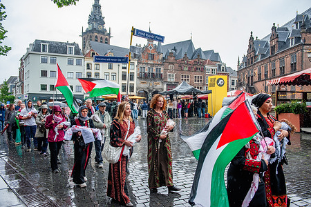 People are marching with Palestinian flags under heavy rain. People march in silence with dolls in white sheets and red stains to symbolize the blood of the Palestinian children killed in Gaza.