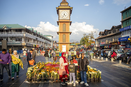 Visitors pose for photos near the clock tower at Lal Chowk surrounded by blooming chrysanthemums during an autumn day in Srinagar.