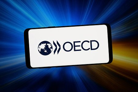 In this photo illustration, the logo of economic development organisation OECD is displayed on a smartphone in front of abstract background on computer screen.