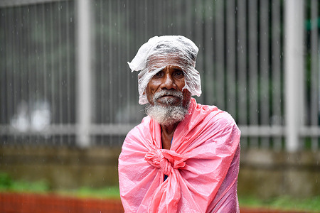 Rickshaw puller Lal Mia standing beside the road waits for passengers during a rainfall in Dhaka.Heavy monsoon downpour caused extreme water logging in most areas of Dhaka city, Bangladesh. Roads were submerged making travel slow and dangerous.