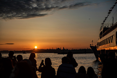 A silhouette of people is seen watching the sunset over the historical peninsula from the Kadikoy quay.
