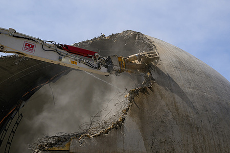A Priestly Demolition high-reach excavator shears through the concrete shell of the historic McLaughlin Planetarium on the University of Toronto . A massive dust cloud fills the interior of the mid-century dome as crews systematically dismantle the landmark for a new academic development