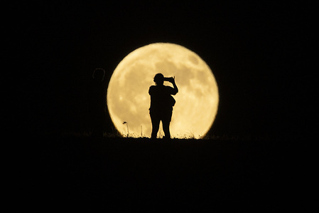 A person is silhouetted while taking pictures as the full moon, also known as the Corn Moon, rises in the sky in Los Angeles.