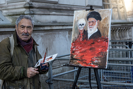 Kaya Mar poses for a photo outside the Downing Street before he carries on with his work about Ali Khamenei. Kaya Mar is London based portrait artist and political satirist. He is very well known for his provocative and satirical paintings. He is outside the Downing Street, London nearly every Wednesday with his newest piece of satire ready to catch MPs after PMQs.