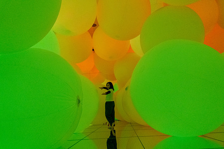 A visitor stands surrounded by glowing, floating spheres inside an immersive digital art installation at teamLab Planets Tokyo in Toyosu, Tokyo, Japan. Created by the art collective teamLab, the interactive environment uses shifting light and color to create a sensory, experiential artwork. teamLab Planets is an immersive digital art museum in Tokyo where visitors walk through interactive installations that blend light, water, and sound. The experience is designed to fully surround the body, creating a constantly shifting environment that responds to movement.