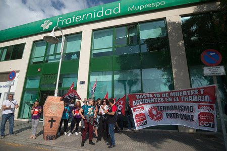 Protesters are seen holding General Confederation of Labour (CGT) flags and a large banner during a protest against workplace accidents in front of a mutual insurance company, before taking part in a tribute to workers who died in labor accidents in the year 2022 in Andalusia. Dozens of people called by the General Workers Conference demonstrated to demand safety measures and accident prevention in the workplace, along with a symbolic homage at the beach.
