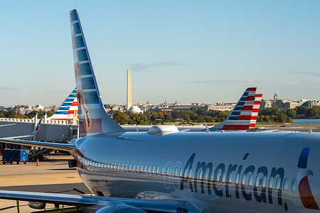 American Airlines jets are parked at gates at Washington Reagan National Airport with the Jefferson Memorial and Washington Monument visible in the background.