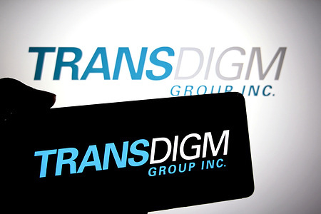 In this photo illustration, a TransDigm Group Inc logo is seen displayed on a smartphone and in the background.