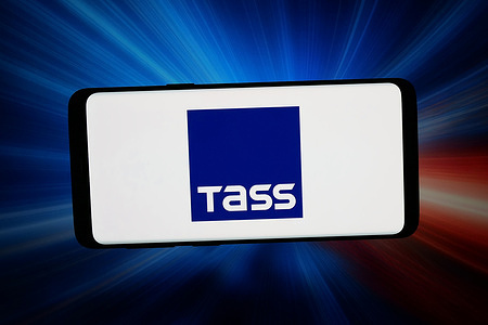 In this photo illustration, the logo of Russian News Agency TASS is displayed on a smartphone in front of abstract background on computer screen.