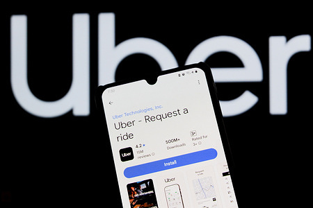In this photo illustration, The Uber logo is seen displayed on a mobile phone and in the background.