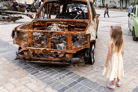 A girl looks at a burned car during an exposition of destroyed Ukrainian civil cars and Russian war vehicles exhibited at Michailovskyi Square in an Old Town of Kyiv. As the Russian Federation invaded Ukraine 3 and a half months ago, fierce fighting continues in the East of the country. The capital, Kyiv stays in relative safety, though reminders of the war such as protective sand bags, road blocks, national and anti-war symbols are present all over the city.