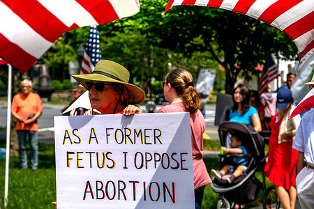 A woman holds placard that says, “As a Former Fetus I Oppose Abortion” at a Pro-choice rally.
