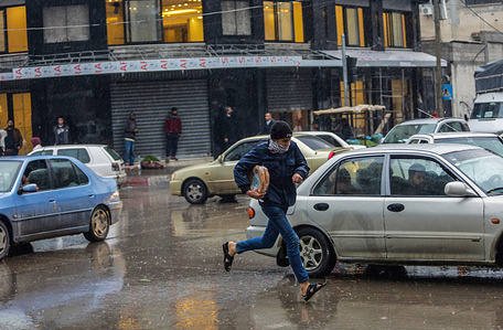 A Palestinian kid is seen running on the street on a rainy day.