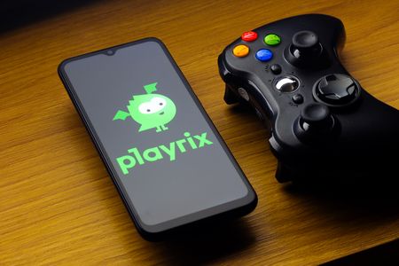 In this photo illustration, the Playrix Entertainment logo is seen displayed on a smartphone screen next to an Xbox video game controller.