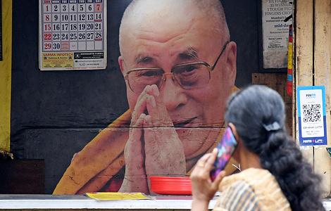A woman talking on her mobile phone walks past a poster of Tibetan Buddhism's spiritual leader. Tibetan Buddhism spiritual leader, His Holiness the 14th Dalai Lama will be celebrating his 90th birthday on 6th July 2025 in Dharamshala in Himachal Pradesh.