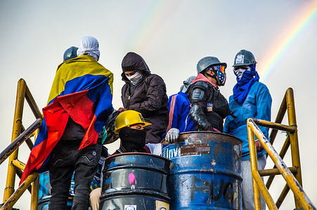 Members of the front line are seen on top of the bridge during a tribute to Jaime Fandiño with a rainbow in the background.
On July 11th in the south of Bogotá, a tribute was organized in memory of Jaime Fandiño, a 32-year-old man who was hit by a tear gas canister fired directly into his chest by anti-riot police. During the event concerts, graffiti, talks, and a community pot took place. In the two months of protests, 74 people have been killed in Colombia.