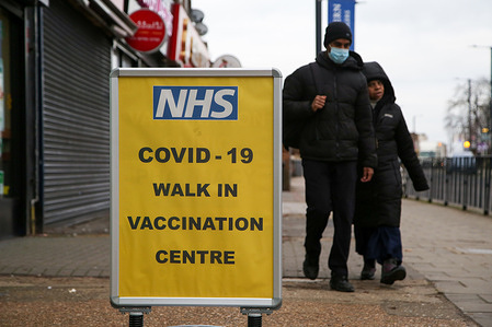 People walk past a vaccination centre sign. 
NHS urges people who tested positive for Covid-19 in December and were unable to get a booster, to get the jab now.