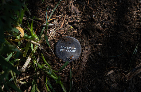A plastic cap with an educational commercial message, "please recycle me," is seen buried in the ground. The cleaning of a rural agricultural garden for private use in Girona reveals the presence of countless remains of decomposing microplastics.
