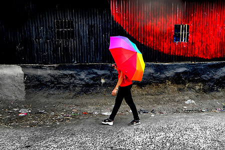 A woman seen walking with a colorful umbrella on the side of a newly painted wall .