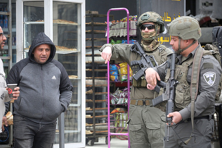 A Palestinian man walks past soldiers guarding the area during a security operation in the al-Ain refugee camp west of Nablus. Israeli forces raided the Hasiba family home in the northern part of the camp and arrested a Palestinian man. Soldiers also stormed shops in the al-Ain refugee camp market.