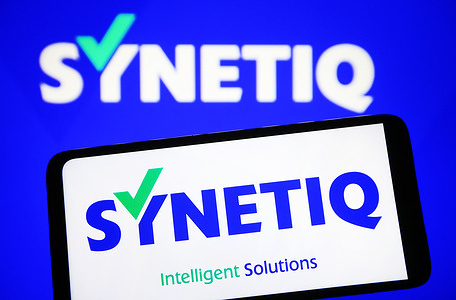 In this photo illustration, Synetiq logo is seen on a smartphone and on a pc screen.