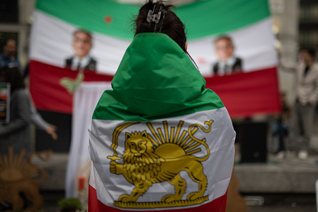 A woman drapped in an Iranian flag looks at a banner with portraits of Reza Pahlavi, Crown Prince of Iran. Iranian residents in Madrid celebrate the Persian New Year, Nowruz 2585, at the Puerta del Sol. Nowruz 2585 marks the beginning of the Persian New Year on the spring equinox of 2026. The number 2585 corresponds to the imperial calendar (Shahanshahi), which counts the years from the founding of the Achaemenid Empire by Cyrus the Great, and coincides with the year 1405 of the Hijri solar calendar.
