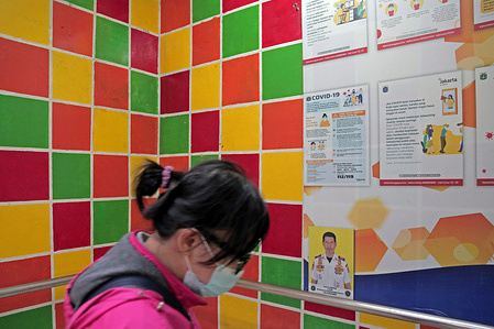 A woman wearing a face mask walks past a Coronavirus disease (COVID-19) warning signpost in Jakarta.