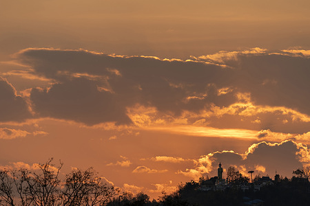 Warm orange hues from the setting sun illuminate scattered clouds above the silhouette of a Buddha statue and temple complex at Wat Phra That Doi Kham in Chiang Mai.