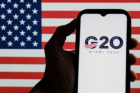In this photo illustration, the 2026 Group of Twenty (G20) Miami Summit logo is seen displayed on a smartphone screen, and the United States of America flag in the background.