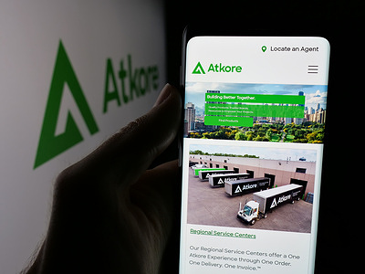 In this photo illustration, a person is holding a smartphone with the web page of US electrical company Atkore Inc. on screen in front of logo.