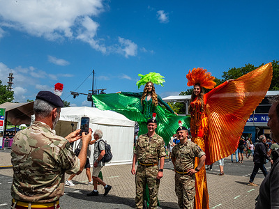 Two female acrobats dressed in the official colors of the walk are posing with military officers. Around 47,000 participants (including the Armed Forces from other countries) registered for the International Four Days Marches (Vierdaagse), the largest multi-day walking event in the world. Walkers picked up their wristbands with the number of registrations at the start point of the walk.