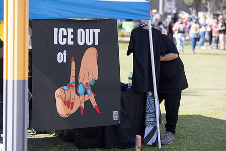 A sign reading “ICE OUT of LA” with illustrated hands forming the letters “L-A” is displayed under a canopy tent, with people gathered in the background. No Kings protest, in front of City Hall, downtown Los Angeles, March 28, 2026.