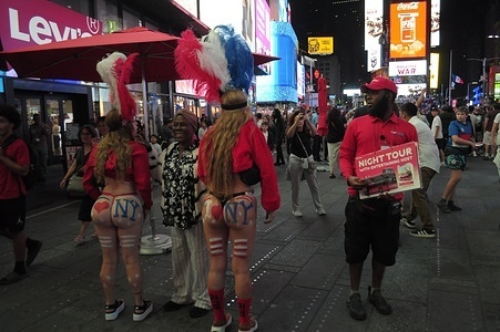 Painted women wearing thongs and costumes, left, take a photo with a pedestrian in Times Square, Manhattan, New York City.